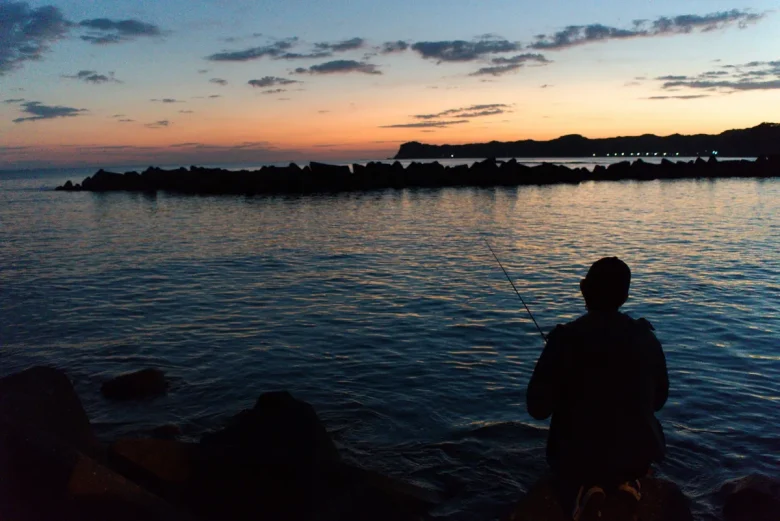 夕暮れの堤防で釣りをする人のシルエット