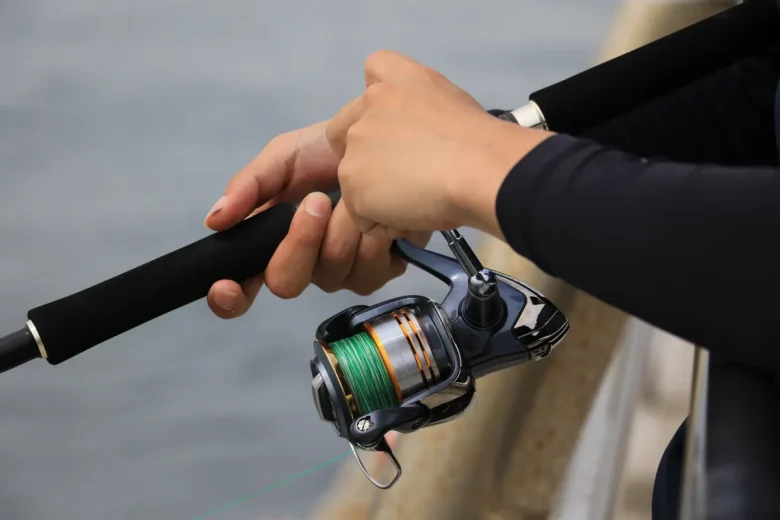 Hands working a spinning reel on a jigging rod at the boat rail